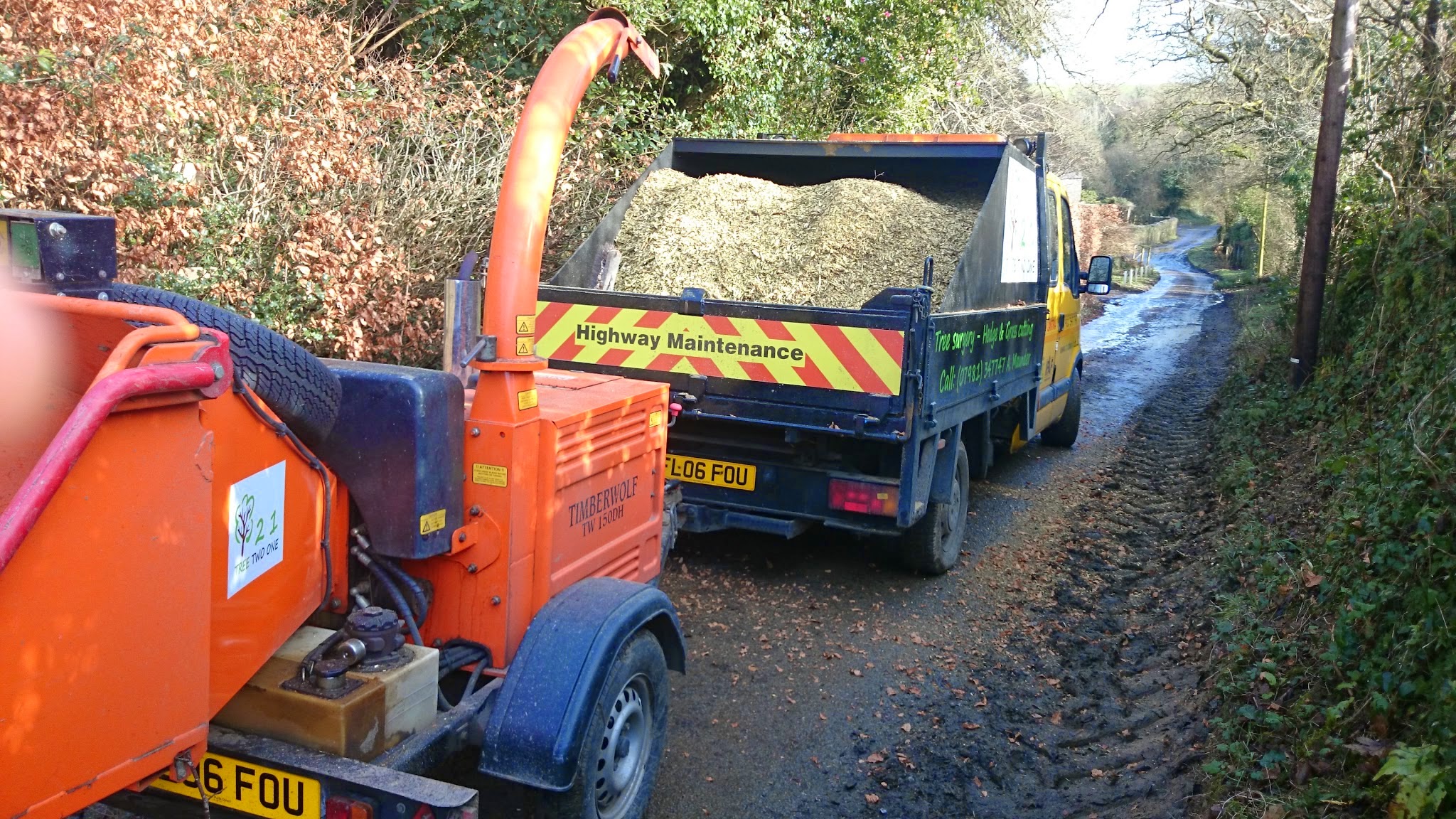 Orange wood chipper and a tipper truck full of chip on a country lane